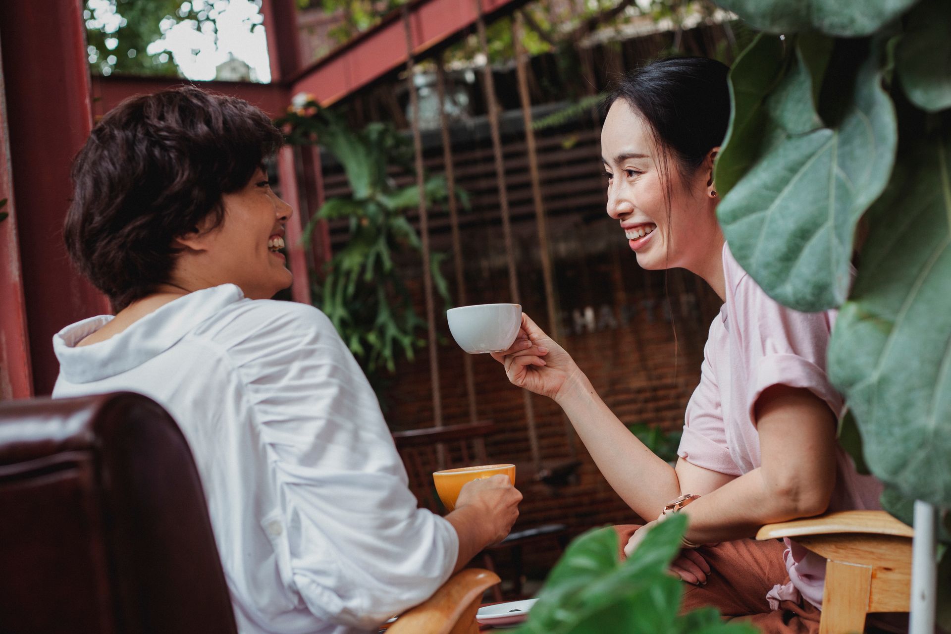 A woman with a bright, confident smile looking happily at her friend in a cozy indoor setting.